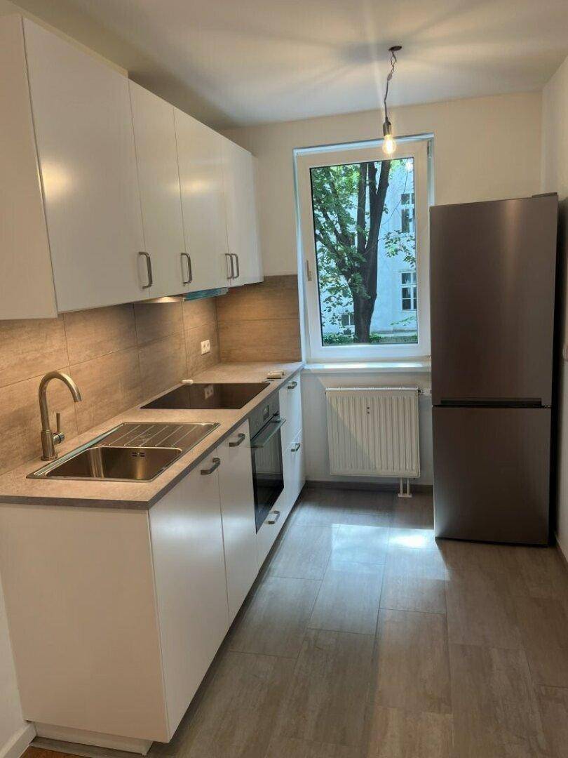 Moderne Küche mit weißen Schränken, integrierten Geräten und einem Fenster mit Blick ins Grüne.