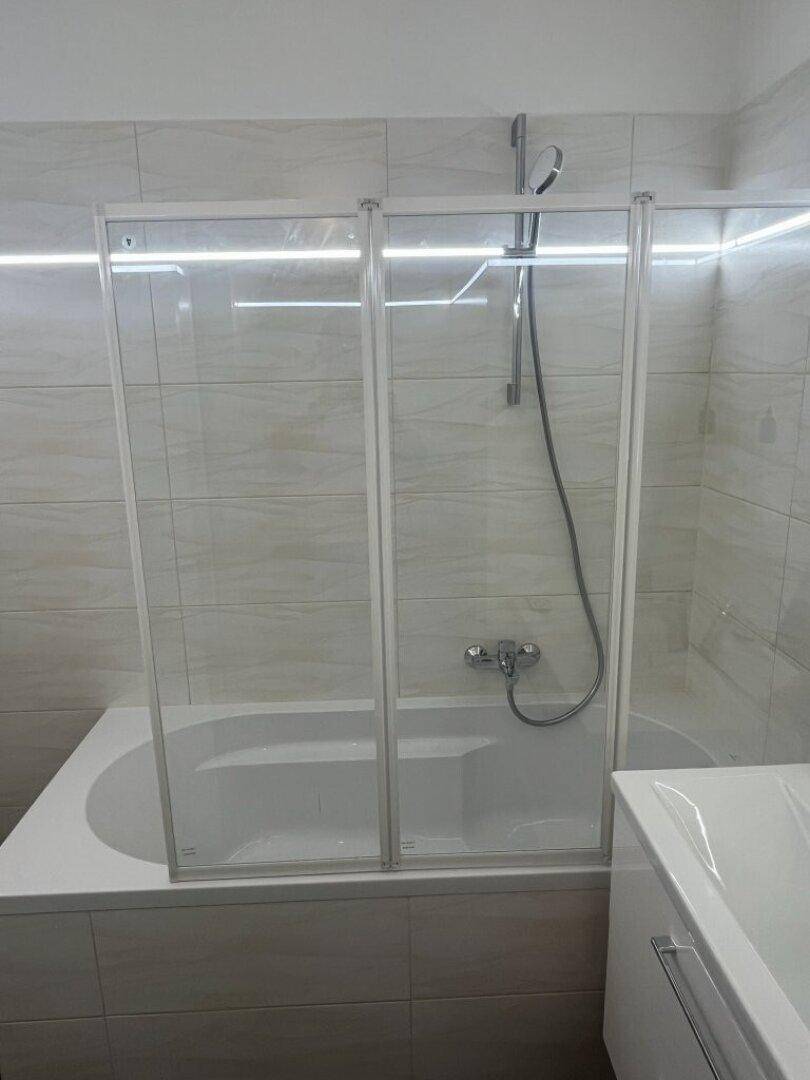 Badewanne mit Glasduschabtrennung in einem hell gefliesten Badezimmer, sauber und funktional gestaltet.