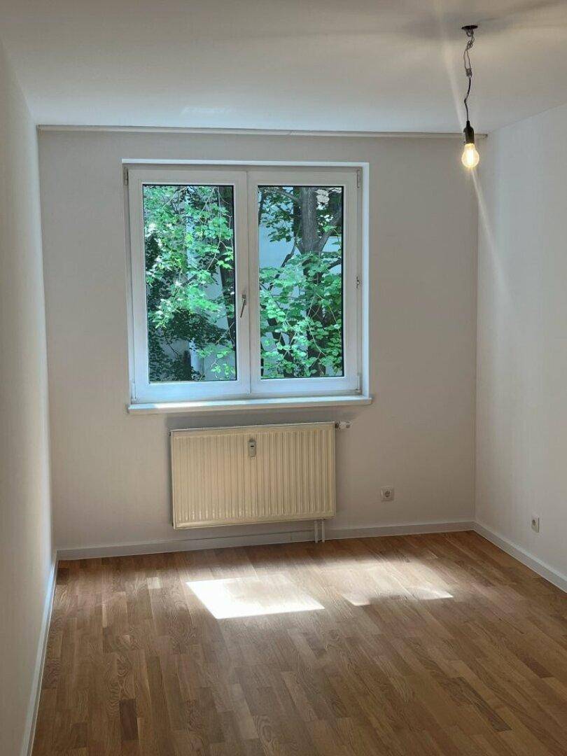 Geräumiges Schlafzimmer mit Parkettboden und großem Fenster, das einen Blick ins Grüne bietet.