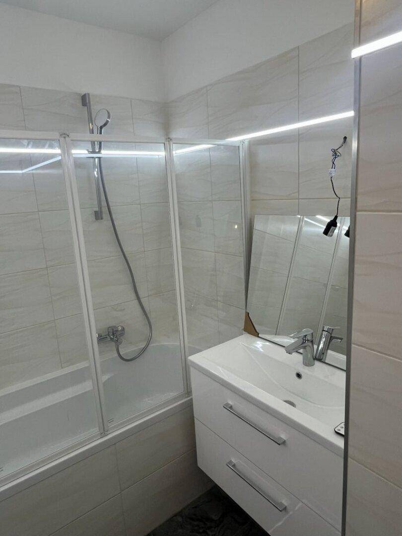 Helles Badezimmer mit Badewanne, Duschabtrennung und modernem Waschtisch, gut beleuchtet und funktional.