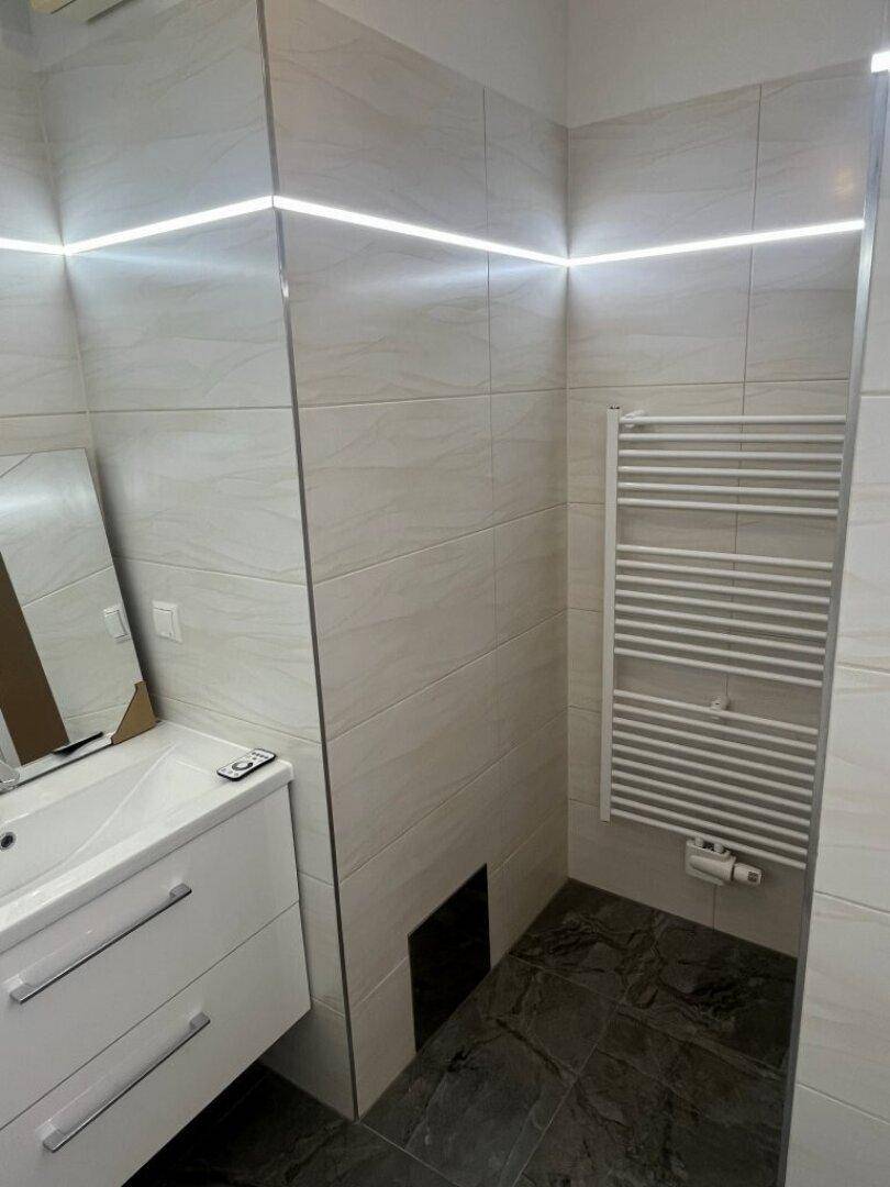 Modernes Badezimmer mit Waschtisch, Spiegel und beheiztem Handtuchhalter, mit dunklem Boden und hellen Fliesen.