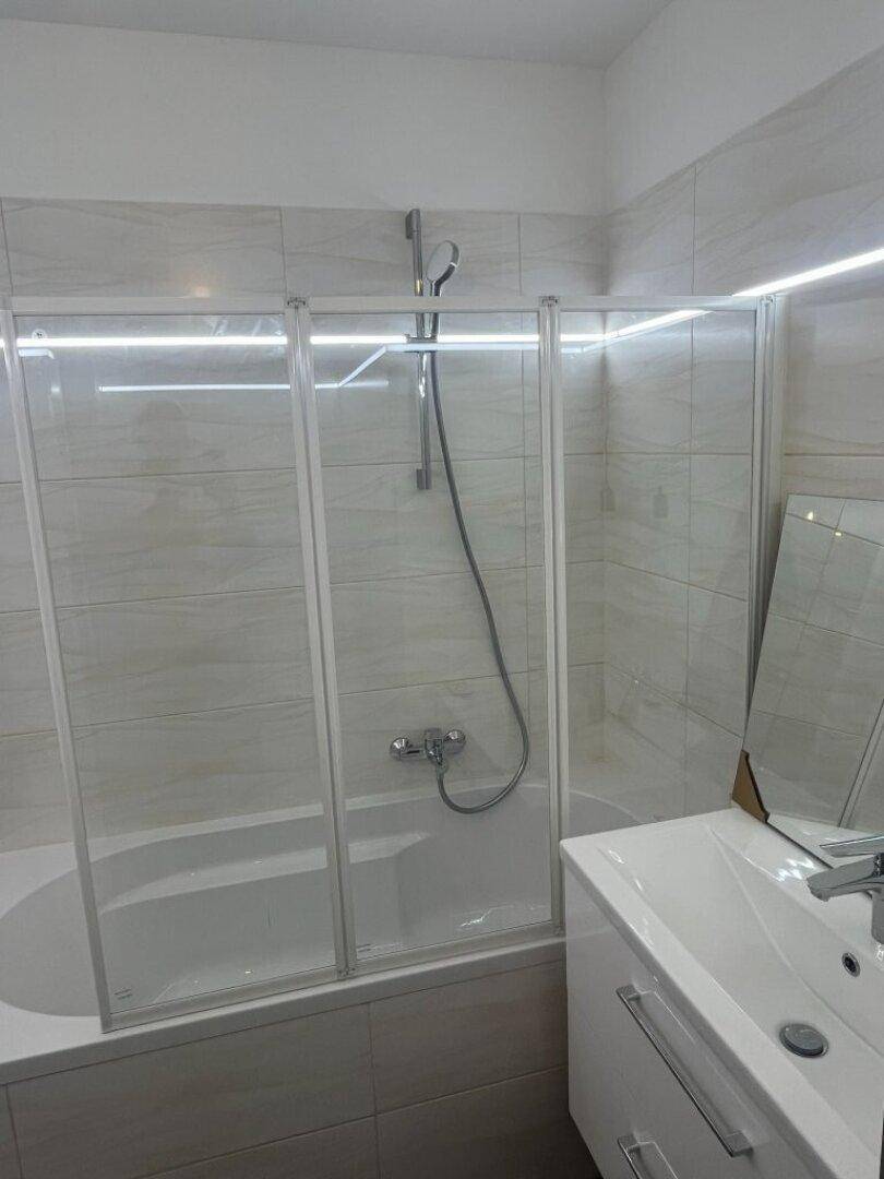 Modernes Badezimmer mit Badewanne, Duschabtrennung und Waschtisch, hell gefliest und gut beleuchtet.
