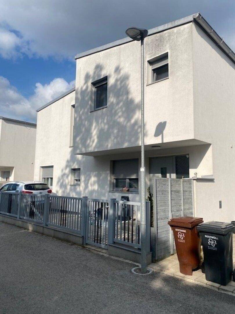 Moderne Reihenhäuser mit weißer Fassade und kleinen Fenstern an einer ruhigen Straße.