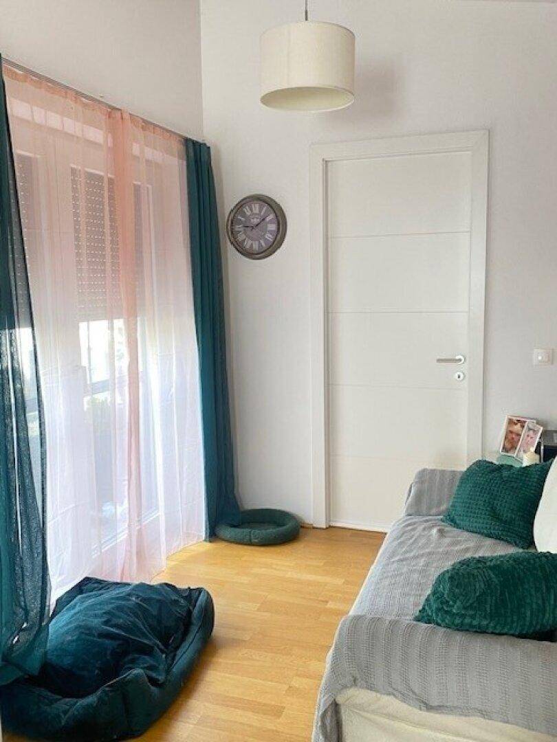 Heller Raum mit Tagesbett, farbigen Vorhängen, großem Fenster und Holzboden.
