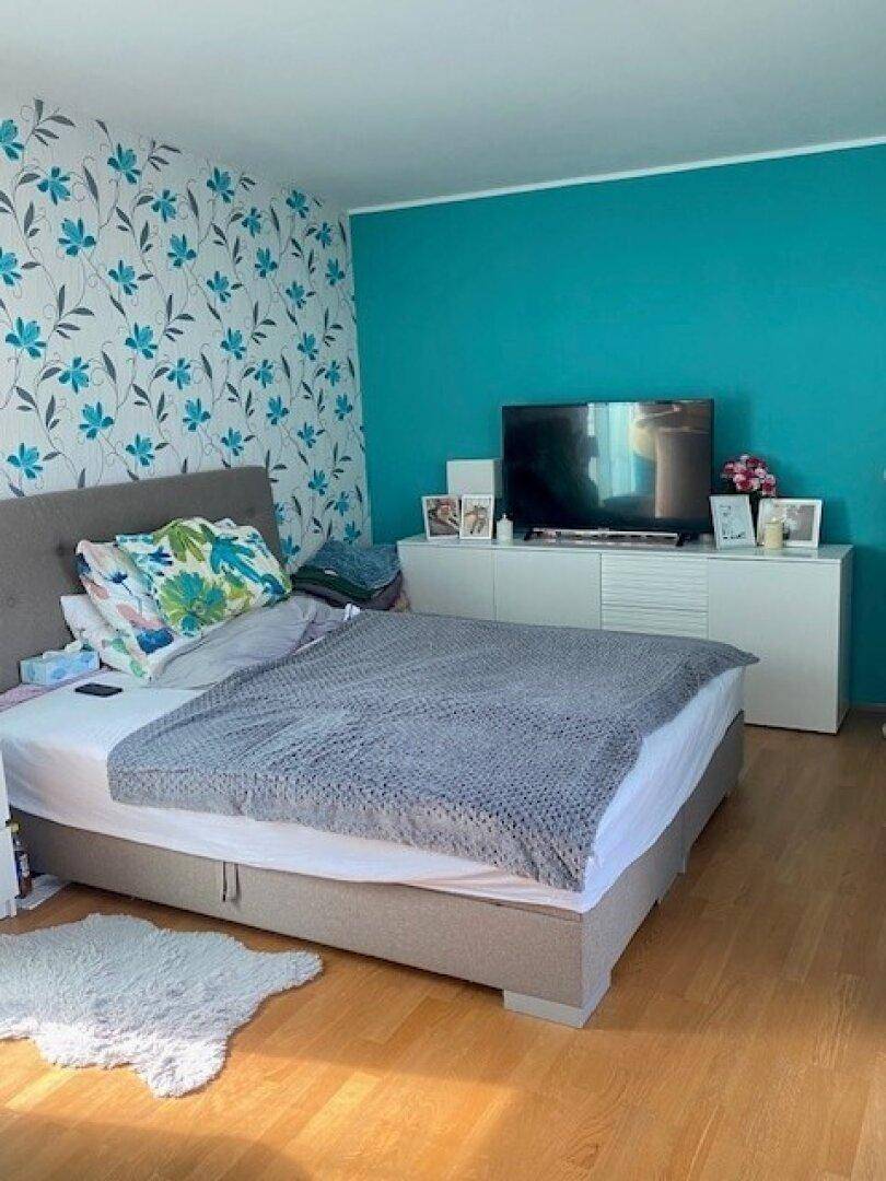 Farbenfrohes Schlafzimmer mit Holzboden, Bett, türkiser Akzentwand und floraler Tapete.