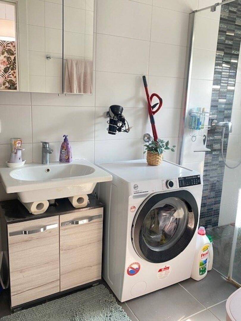 Badezimmer mit Waschbecken, Waschtisch, Waschmaschine und moderner Duschkabine.