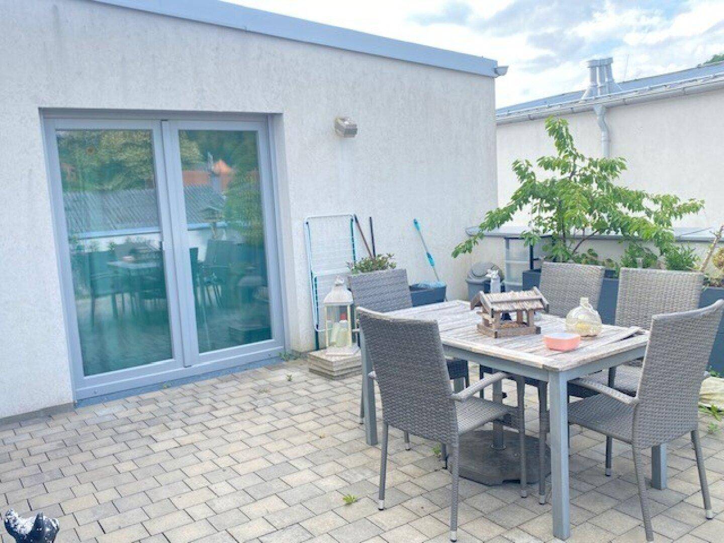 Geräumige Dachterrasse mit Sitzgelegenheiten, Pflasterboden und großer Glasschiebetür.