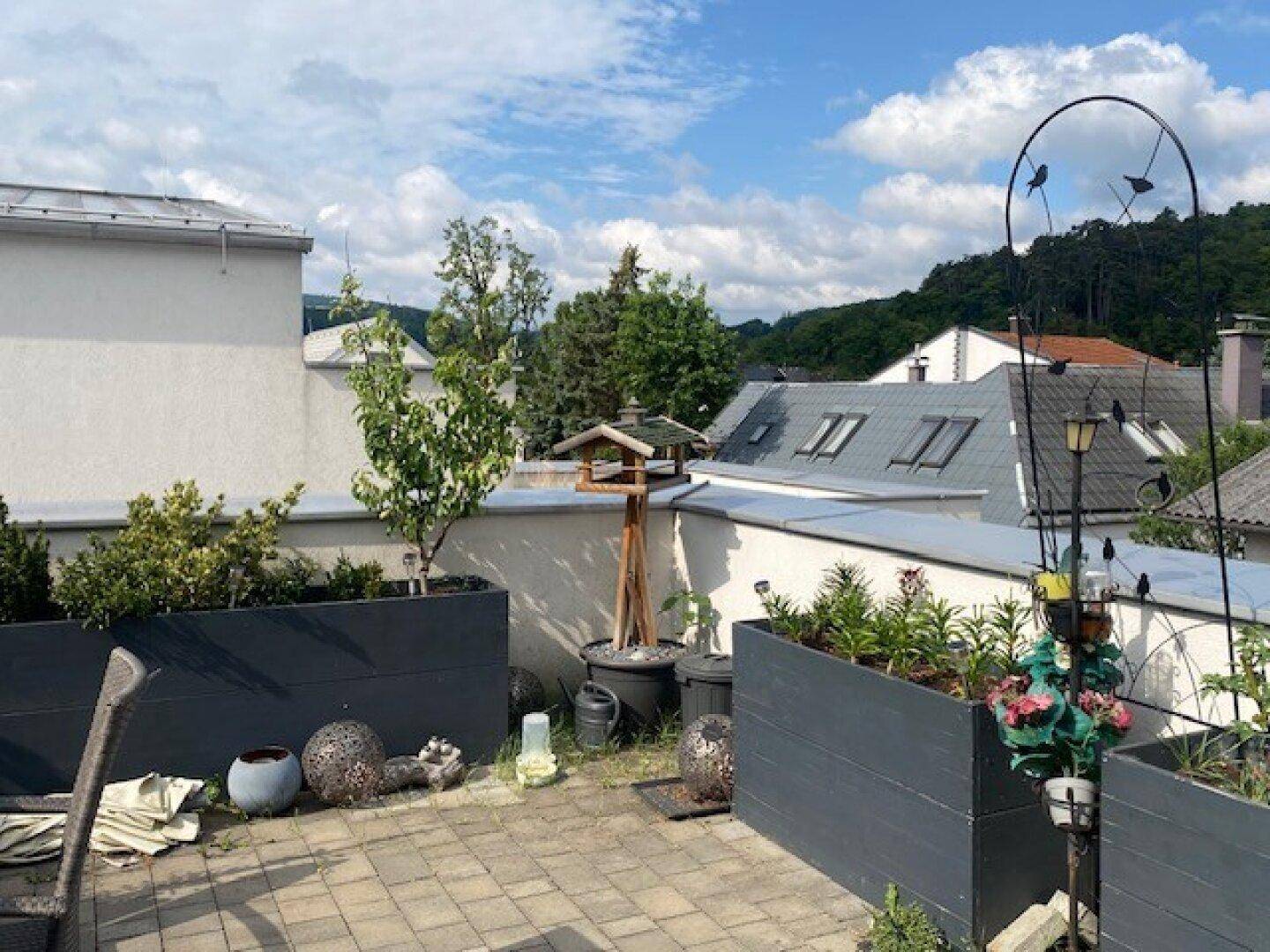 Dachterrasse mit Pflanzkübeln, Dekoration und Blick auf die umliegende Wohngegend und Hügel.