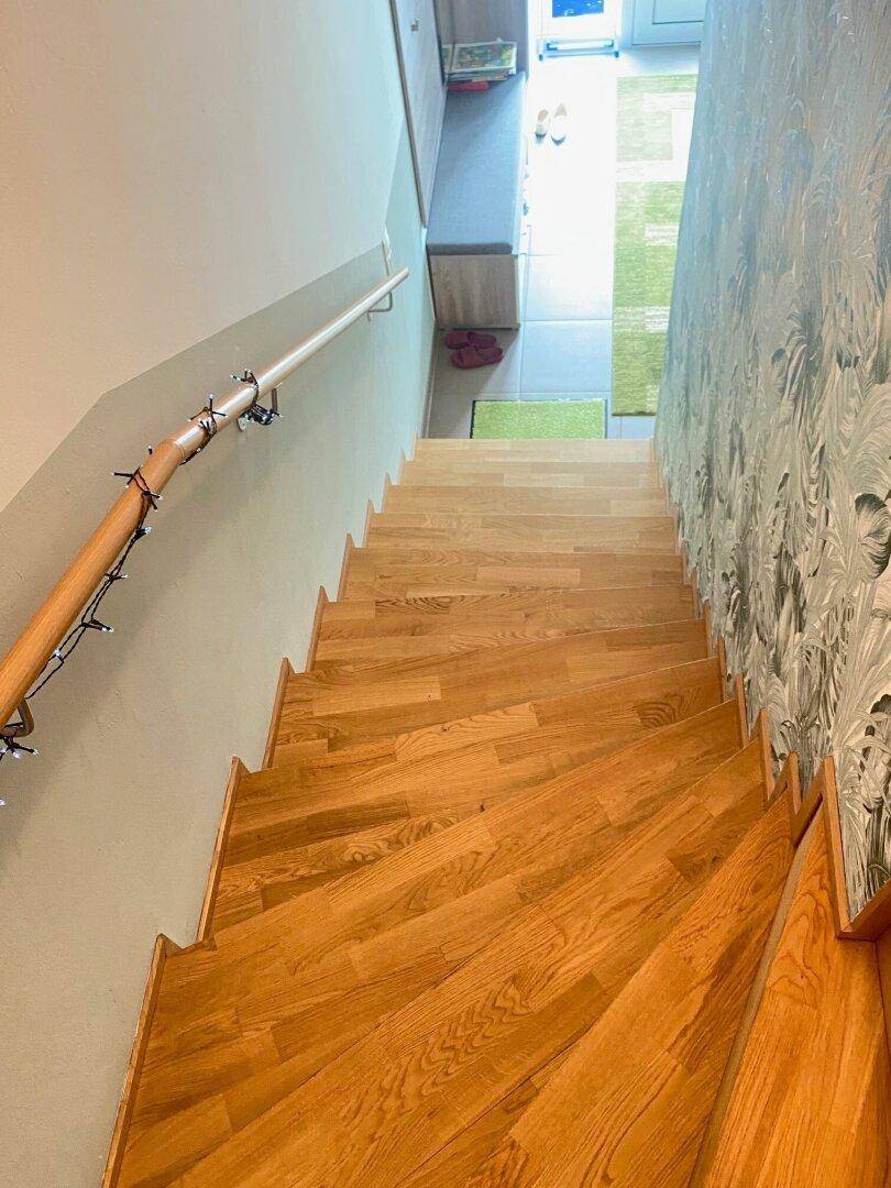 Holztreppe mit Handlauf und dekorativer Beleuchtung, die in den unteren Bereich führt.