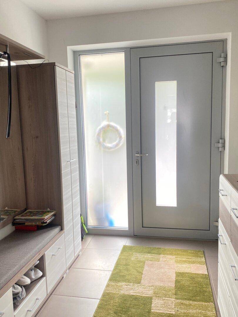 Heller Eingangsbereich mit moderner Haustür, Schuhschrank und Fliesenboden.