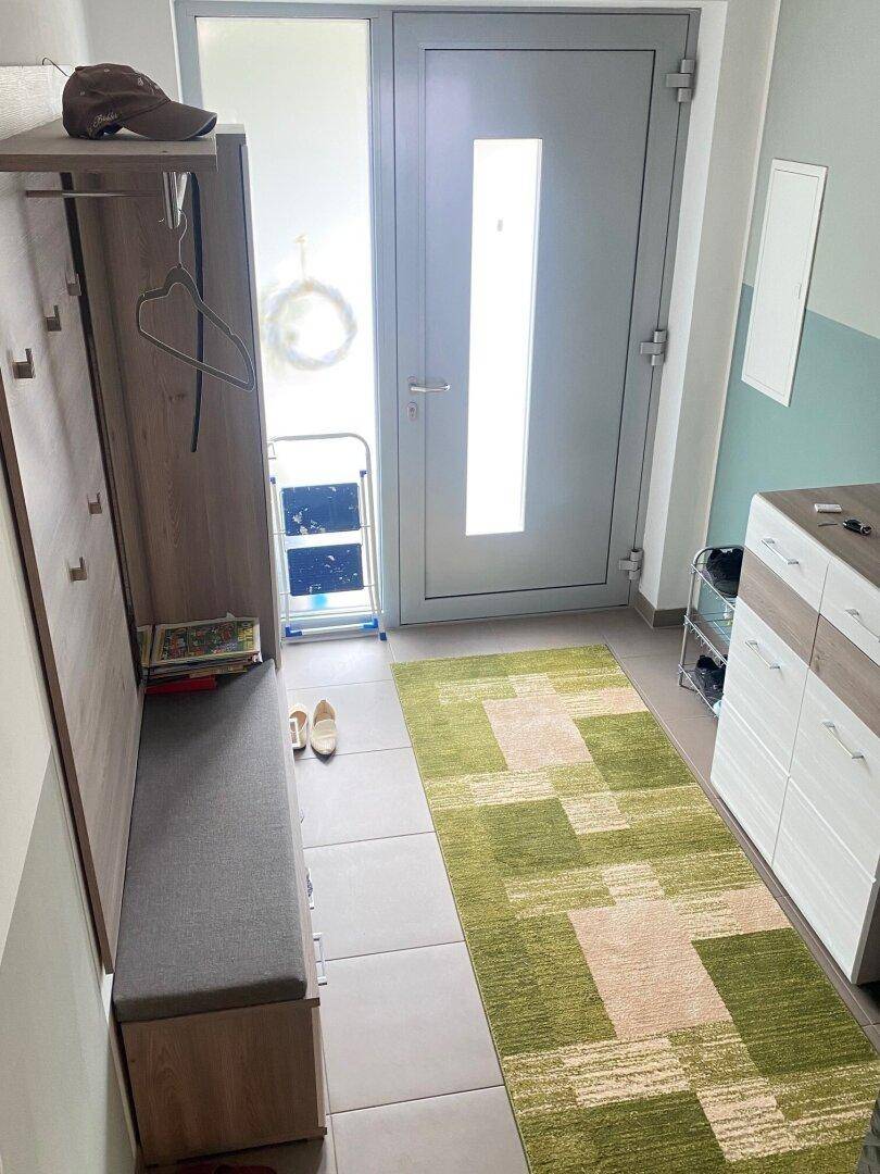 Heller Eingangsbereich mit Garderobe, Schuhschrank und einem modernen grünen Teppich.