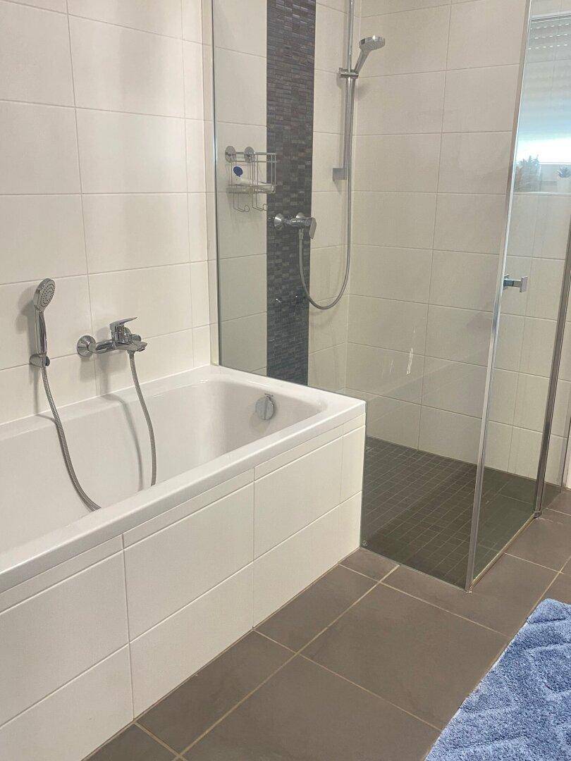 Badezimmer mit Badewanne und Duschkabine, gefliest mit weißen und dunklen Akzentfliesen.