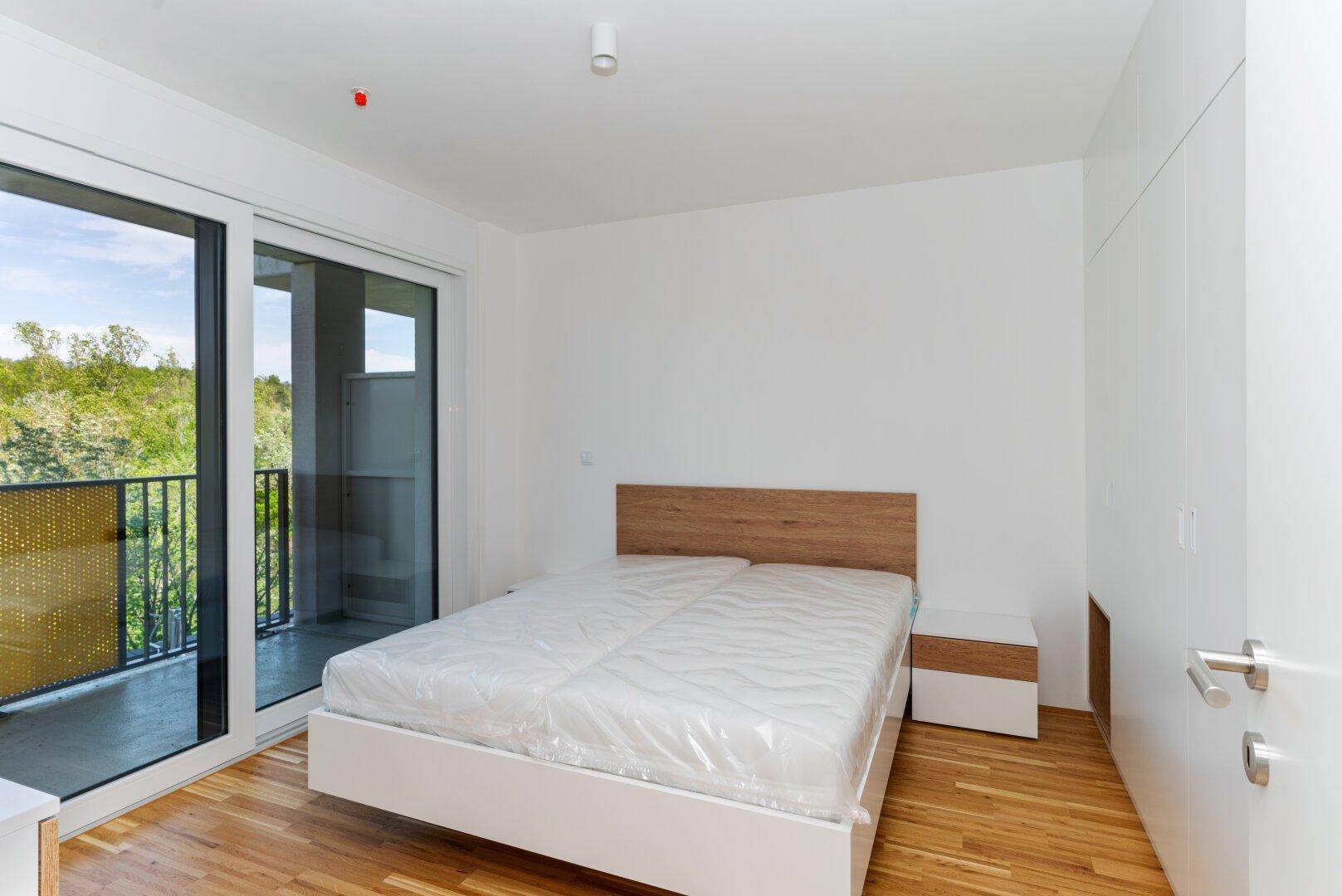 Helles Schlafzimmer mit Doppelbett, Einbauschränken und Zugang zum Balkon.