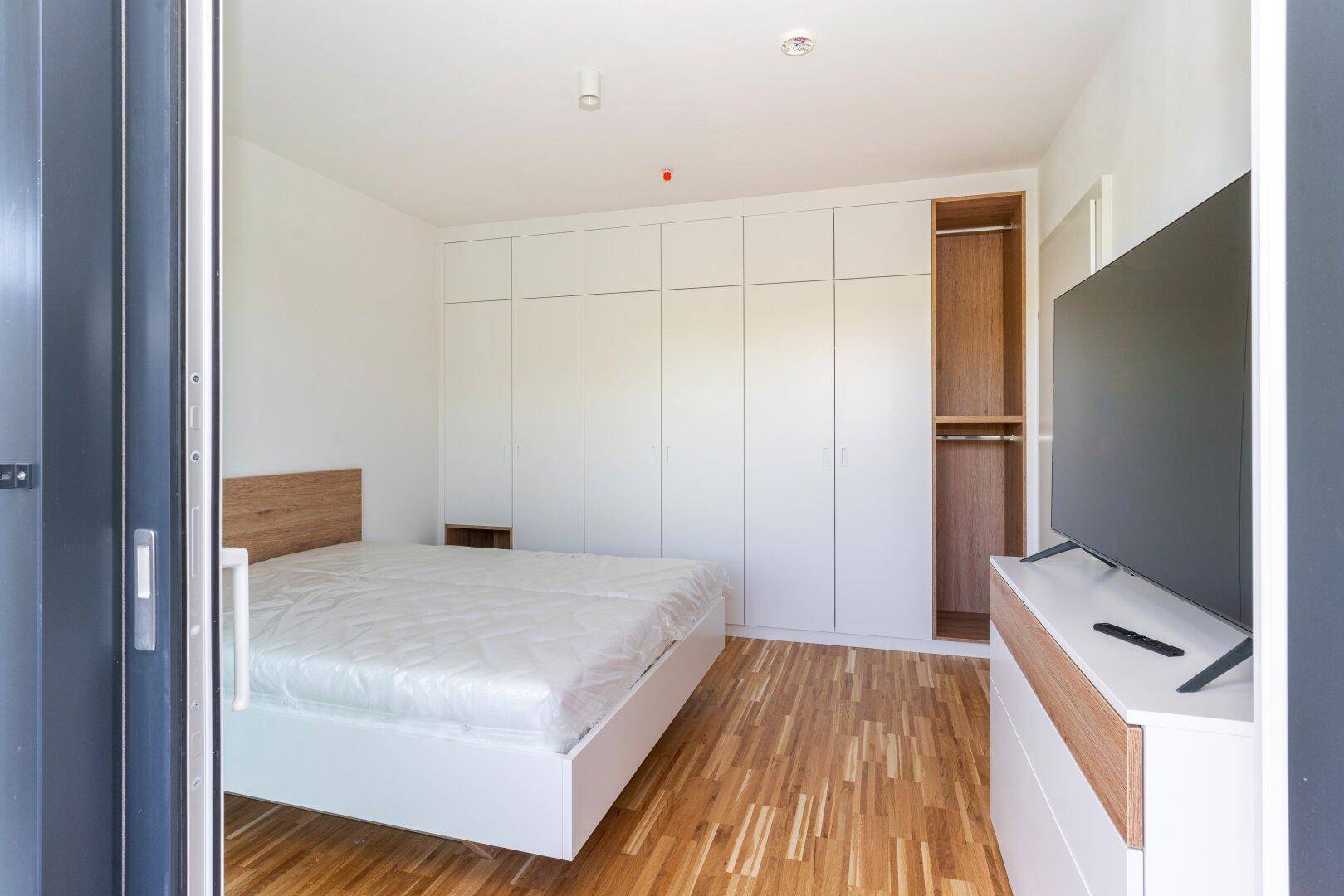Schlafzimmer mit geräumigen Einbauschränken und Blick auf den Balkon.