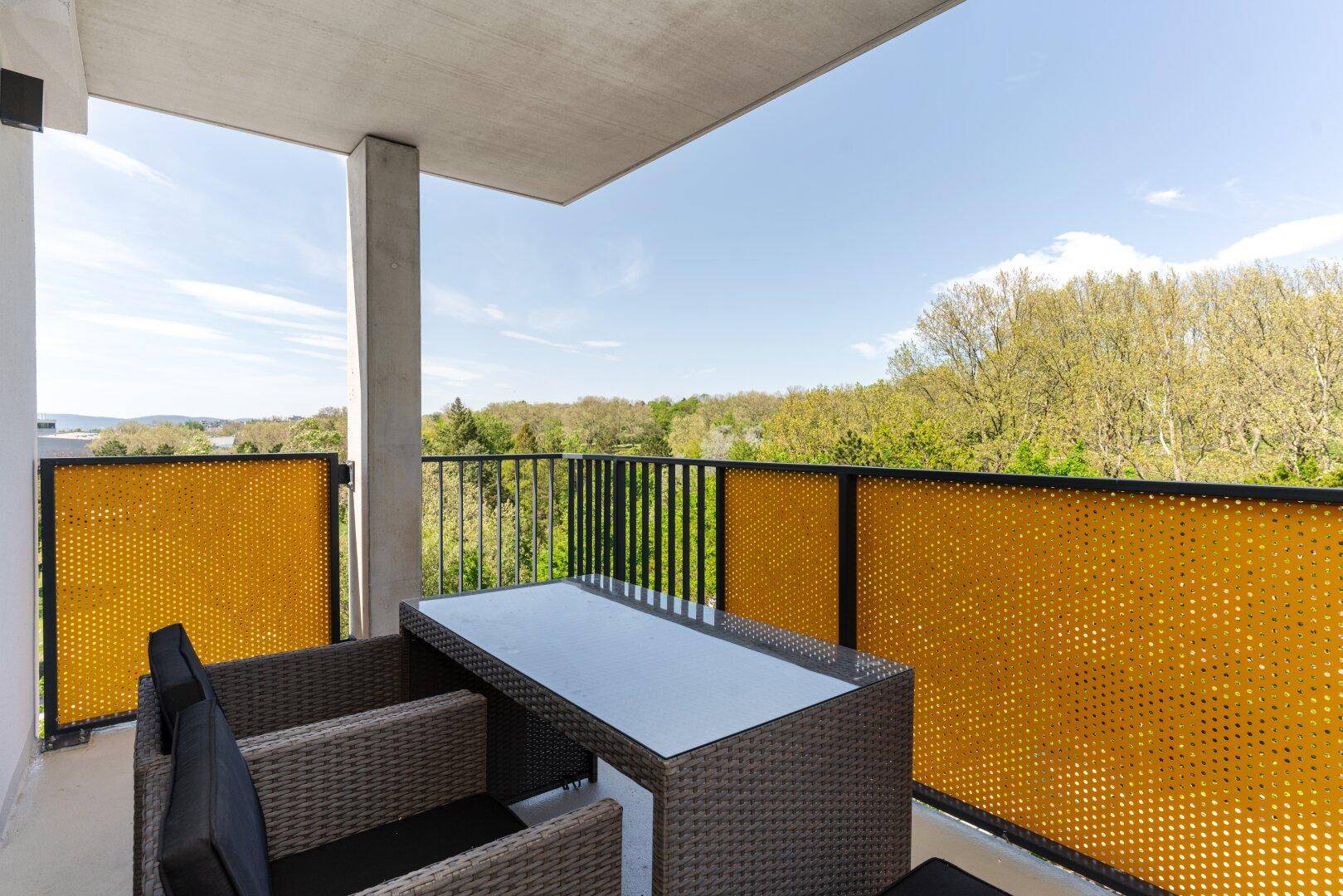 Möblierter Balkon mit Rattan-Sitzgruppe und weitem Blick ins Grüne.