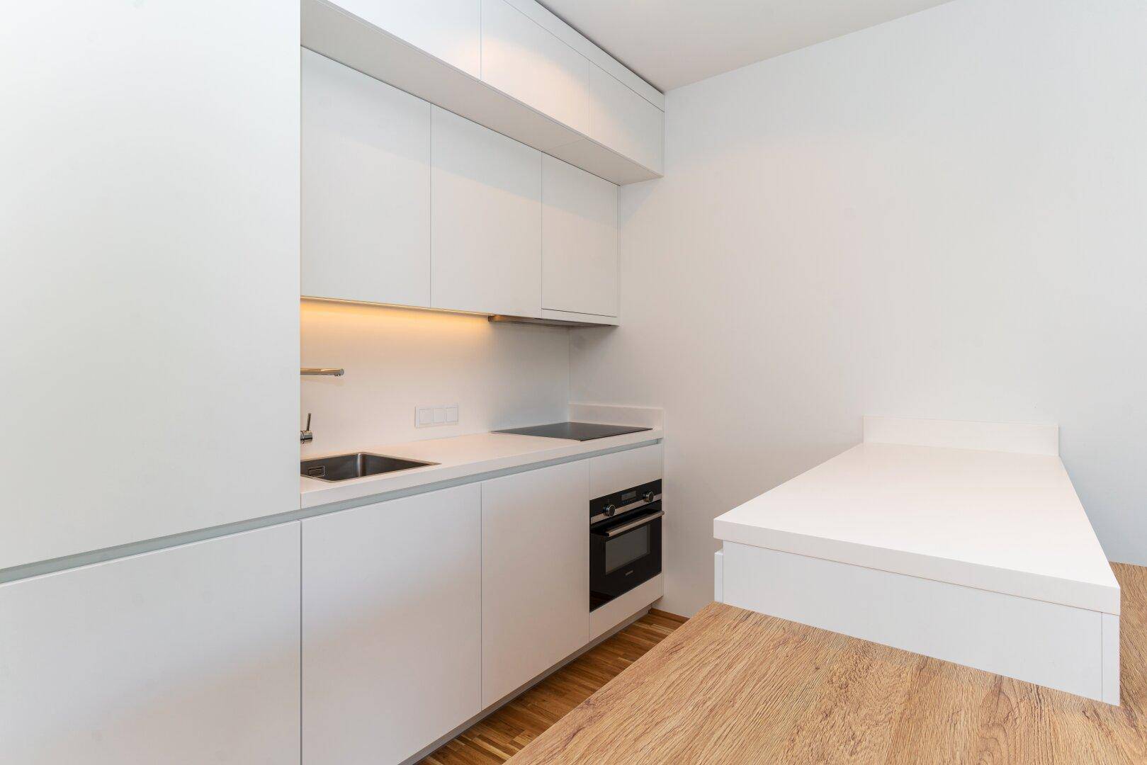 Moderne Küchenzeile mit integriertem Backofen, Spüle und Kochfeld in minimalistischem Design.