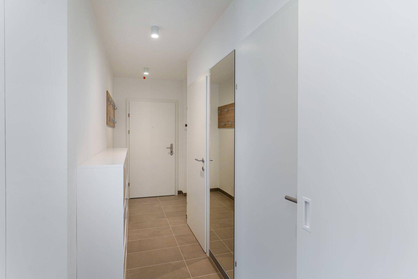 Heller Flur mit Fliesenboden, Spiegeltür und Garderobenschrank im Eingangsbereich.