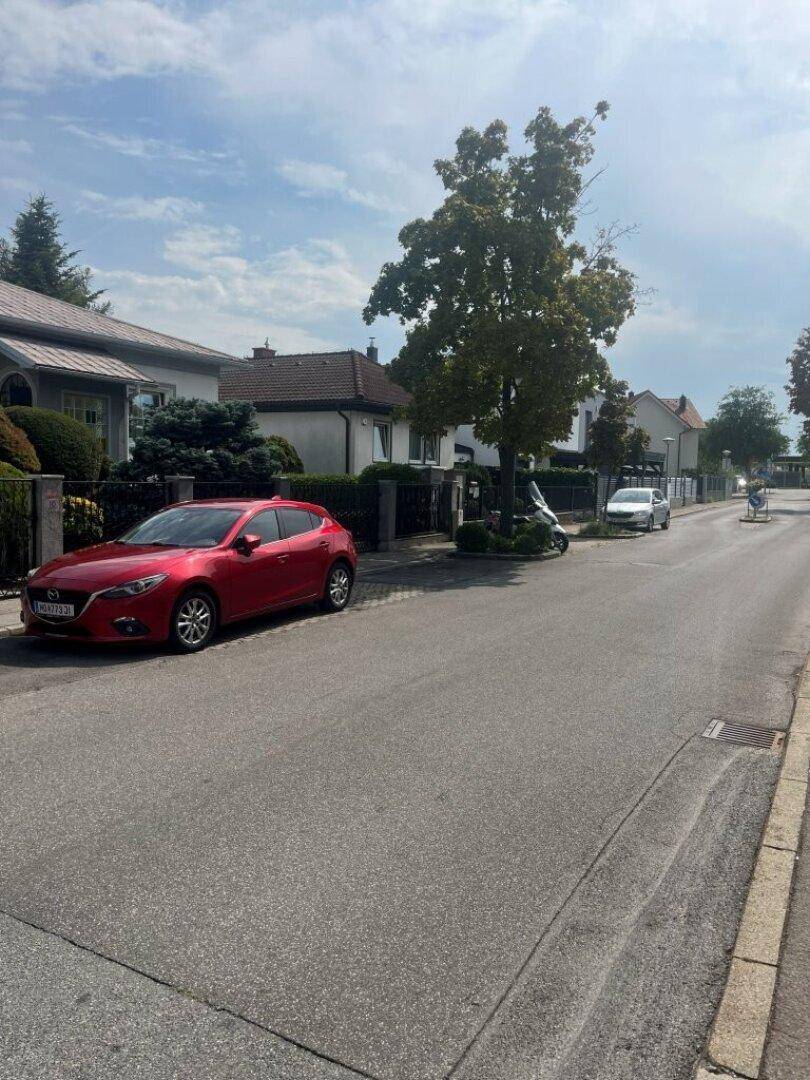 Ruhige Wohnstraße mit geparkten Autos und Bäumen.