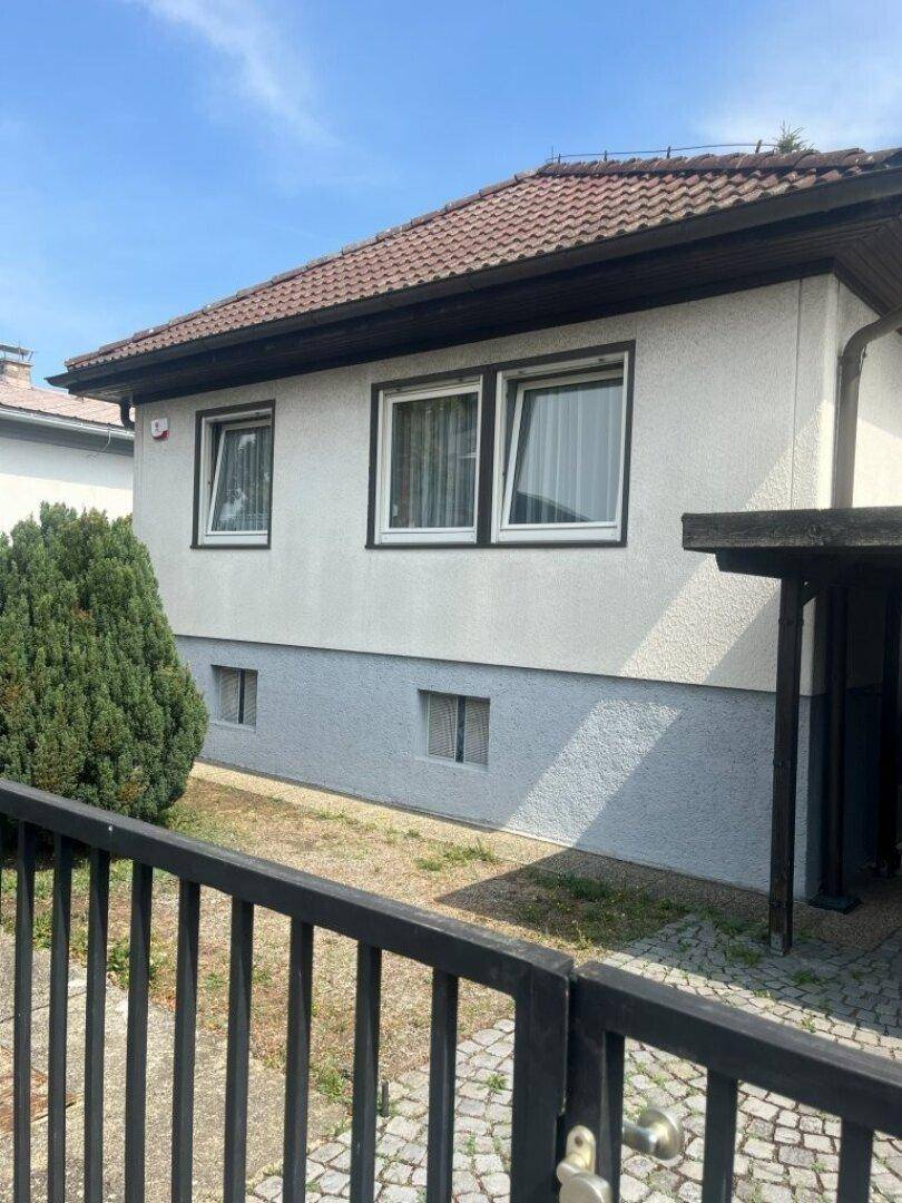 Seitenansicht des Hauses mit heller Fassade, braunem Dach und kleinem Vorgartenbereich.