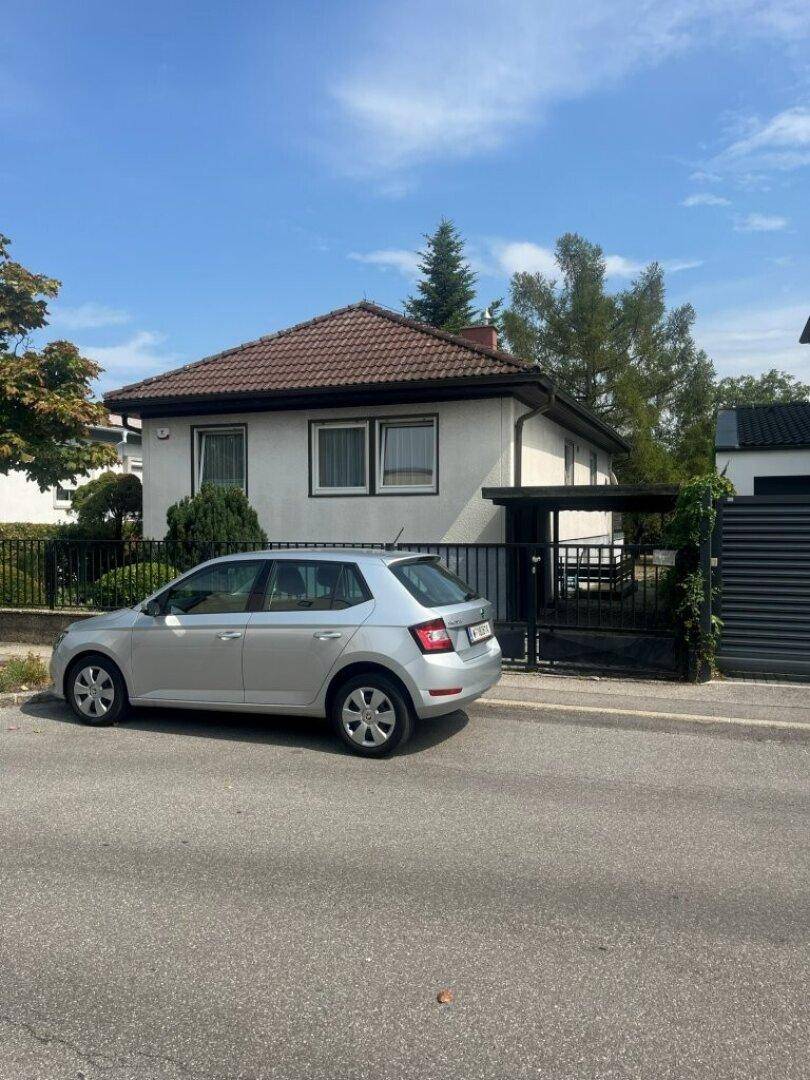 Einfamilienhaus mit heller Fassade und Satteldach, davor ein geparktes Auto auf der Straße.