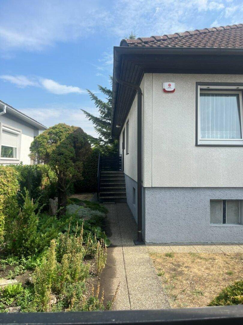 Seitenansicht des Hauses mit Zugangstreppe und gepflegter Bepflanzung entlang des Weges.
