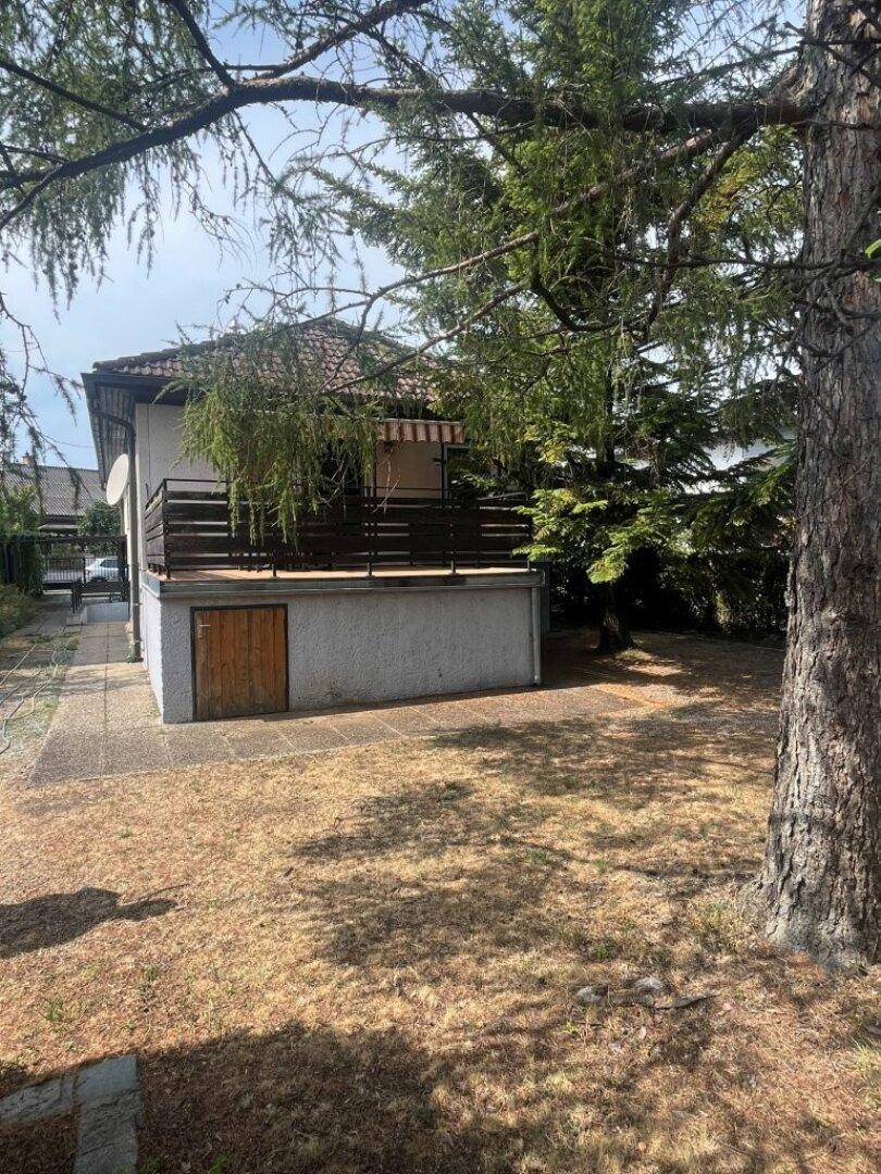 Rückseite des Hauses mit Terrasse, Gartenbereich und hohen Bäumen.