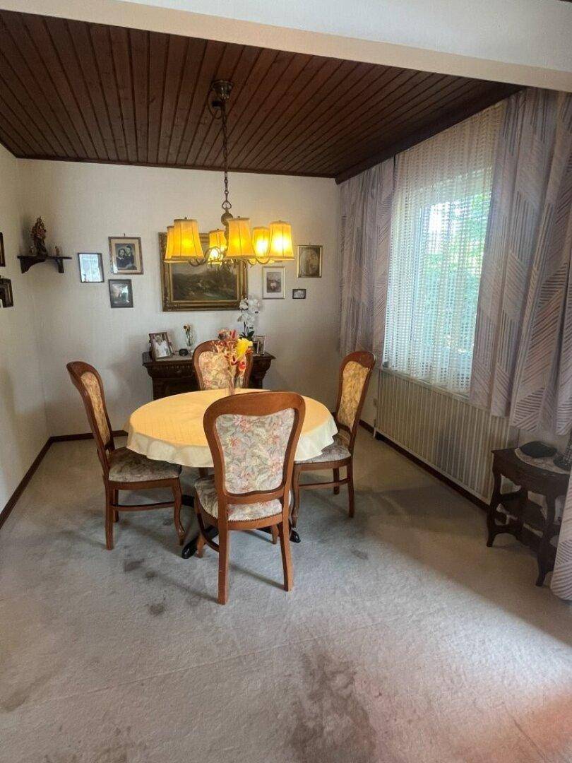 Esszimmer mit Holztäfelung an der Decke, Teppichboden und traditionellen Möbeln.