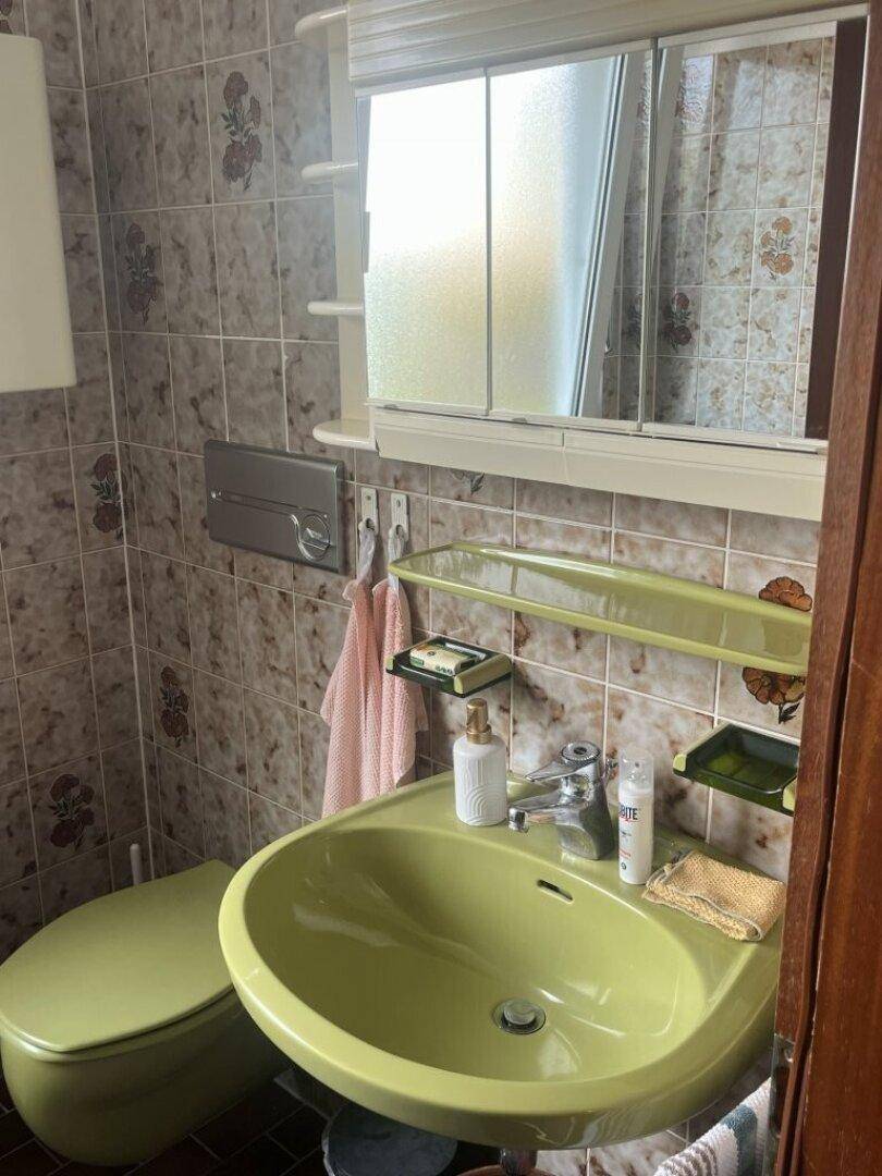 Badezimmer mit grünem Waschbecken, WC und gemusterten Fliesen im Retro-Stil.