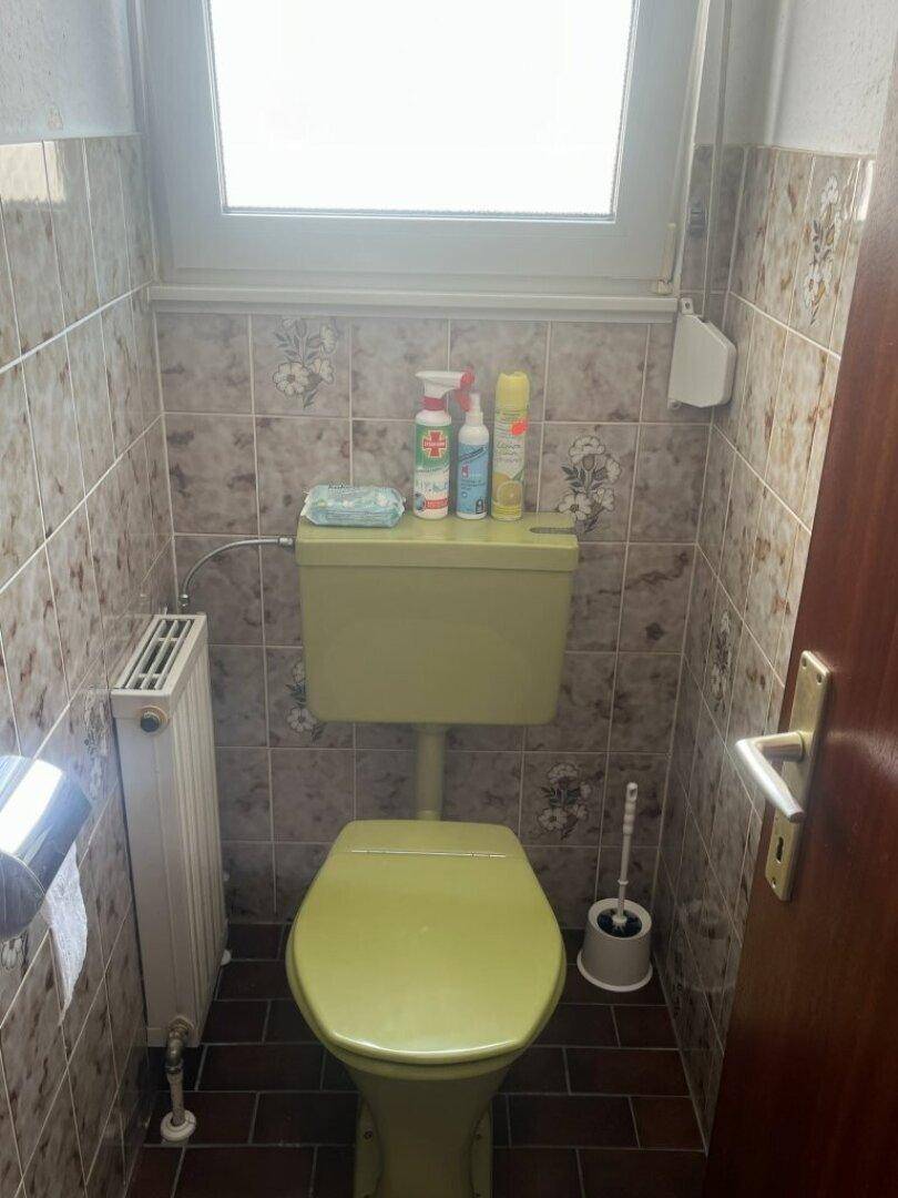 Kleines WC mit Fenster, grünem WC und gemusterten Fliesen im Retro-Stil.