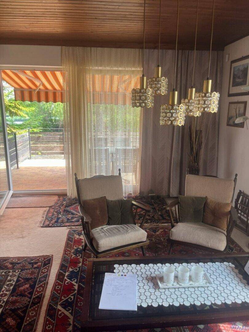 Helles Wohnzimmer mit Zugang zur Terrasse, Teppichboden und dekorativen Leuchten.