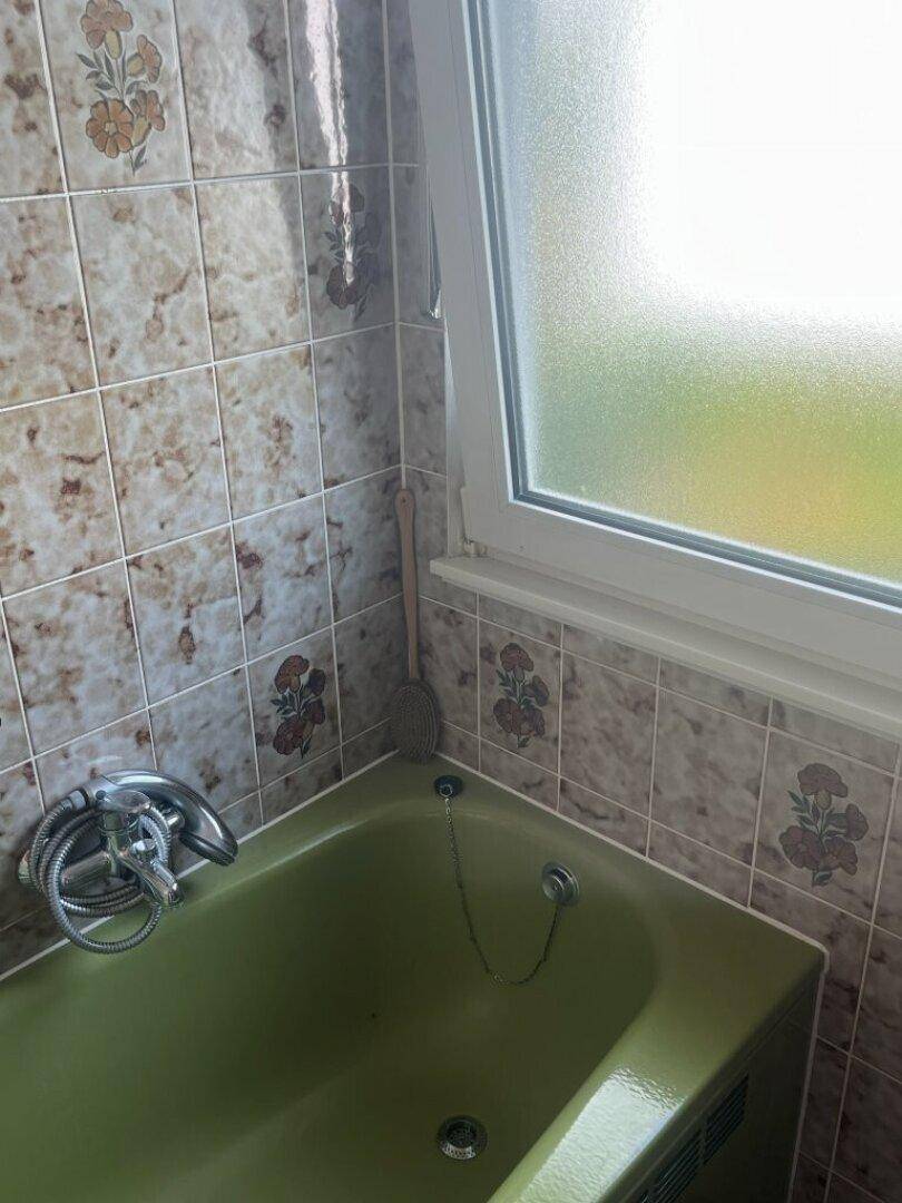 Badezimmer mit grüner Badewanne und Fenster, umgeben von gemusterten Fliesen.