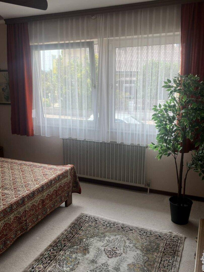Helles Schlafzimmer mit großem Fenster, Heizkörper und Blick nach draußen.