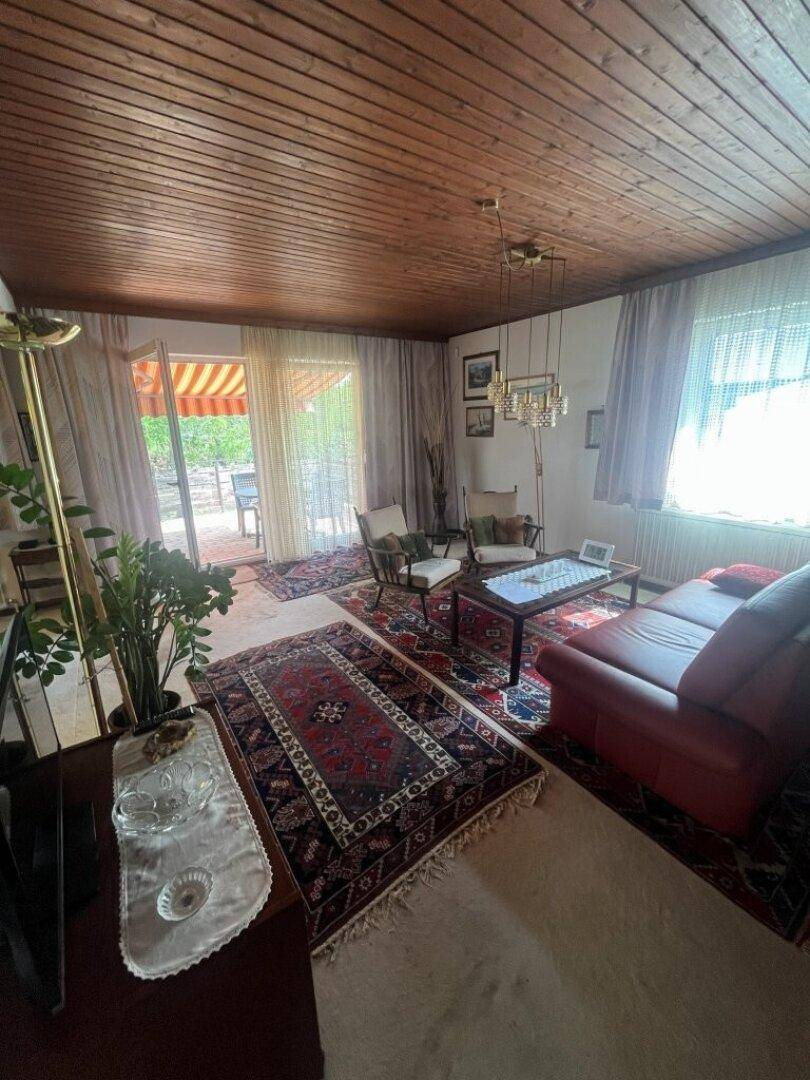Geräumiges Wohnzimmer mit Holzdecke, Teppichen und Zugang zur Terrasse.