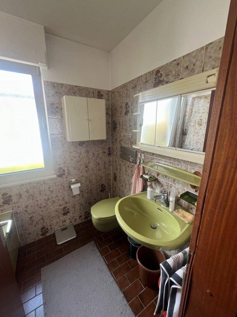 Badezimmer mit grünem Waschbecken, WC und gemusterten Fliesen im Retro-Stil.