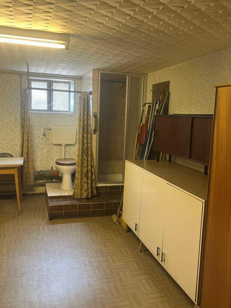 Funktionales Badezimmer im Keller mit Toilette, Duschkabine und älteren Fliesen, einfach ausgestattet.