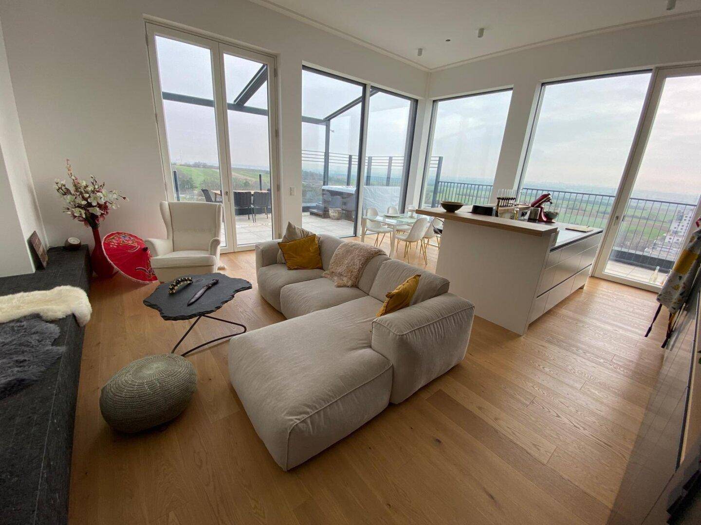 Geräumiger Wohnbereich mit beigem Sofa, Holzboden und Zugang zur Terrasse mit Weitblick.