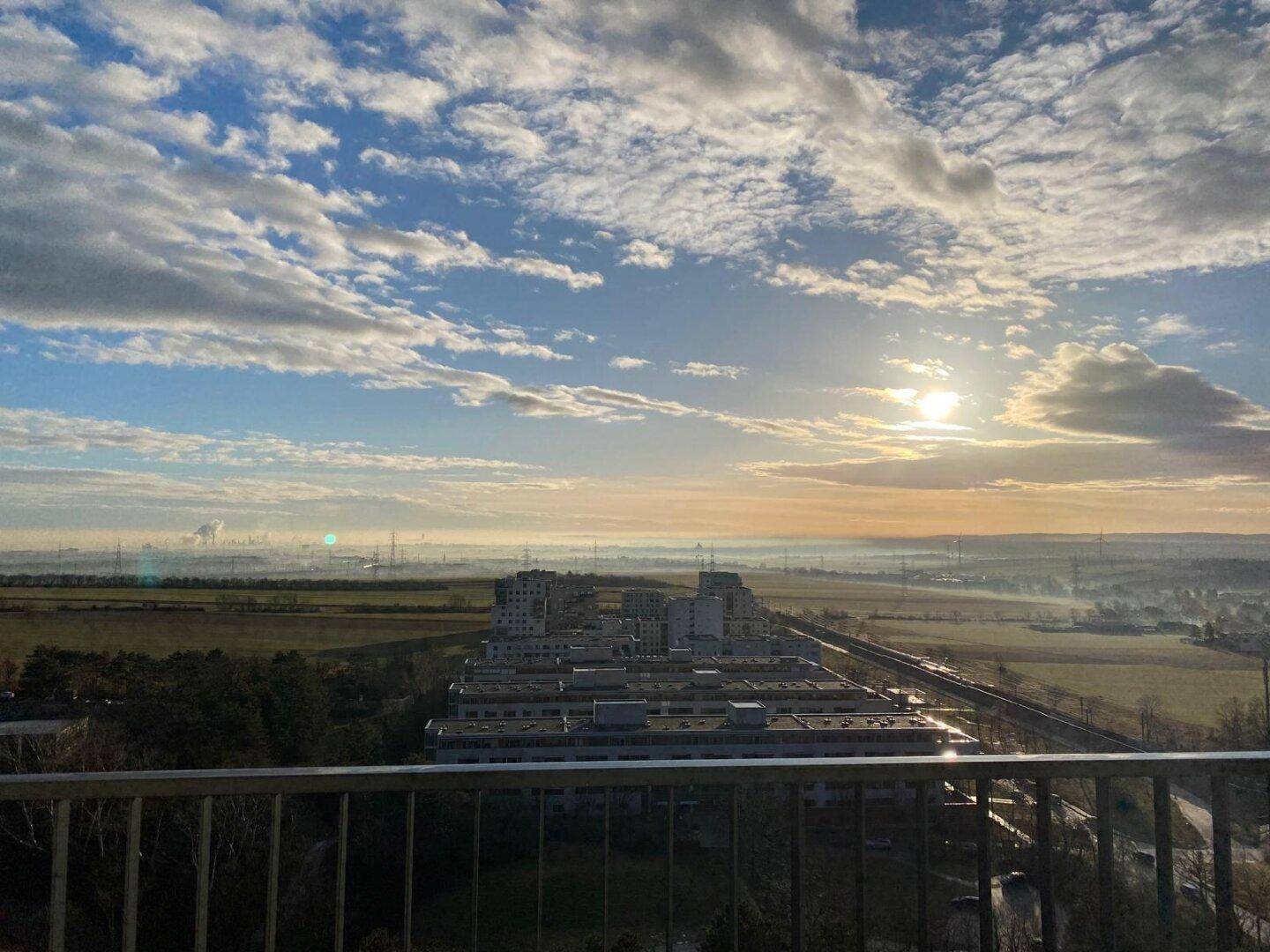 Panoramablick über eine weite Landschaft mit Gebäuden und einem strahlenden Sonnenaufgang.
