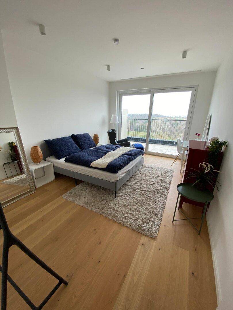 Helles Schlafzimmer mit Holzboden, großem Bett und Zugang zu einem Balkon.