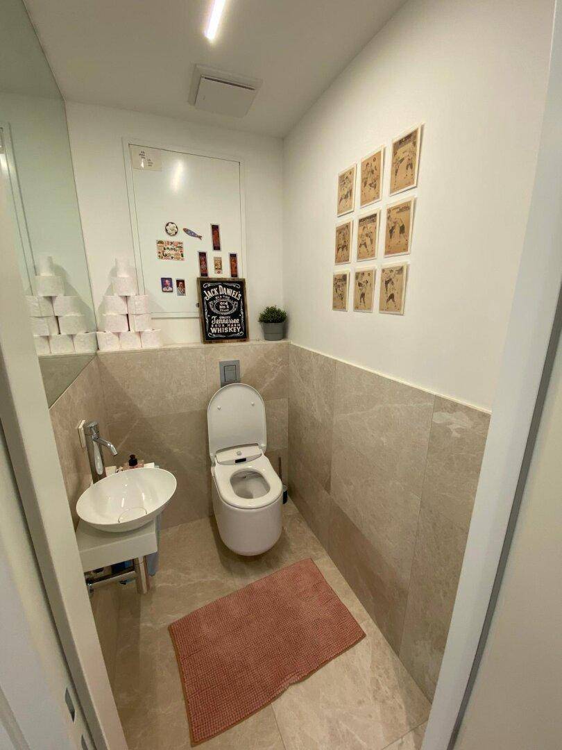 Modernes Gäste-WC mit Wand-WC, kleinem Waschbecken und hellen Fliesen an Wänden und Boden.