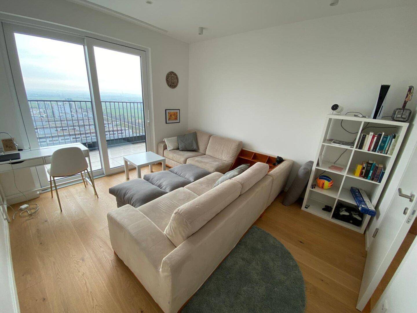 Gemütliches Wohnzimmer mit großem Sofa, Holzboden und Zugang zum Balkon.