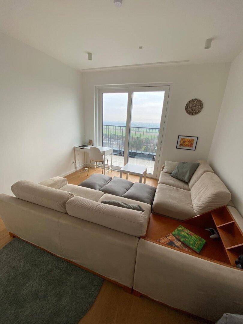 Heller Wohnbereich mit beigem Sofa, Holzboden und Blick auf die umliegende Landschaft.