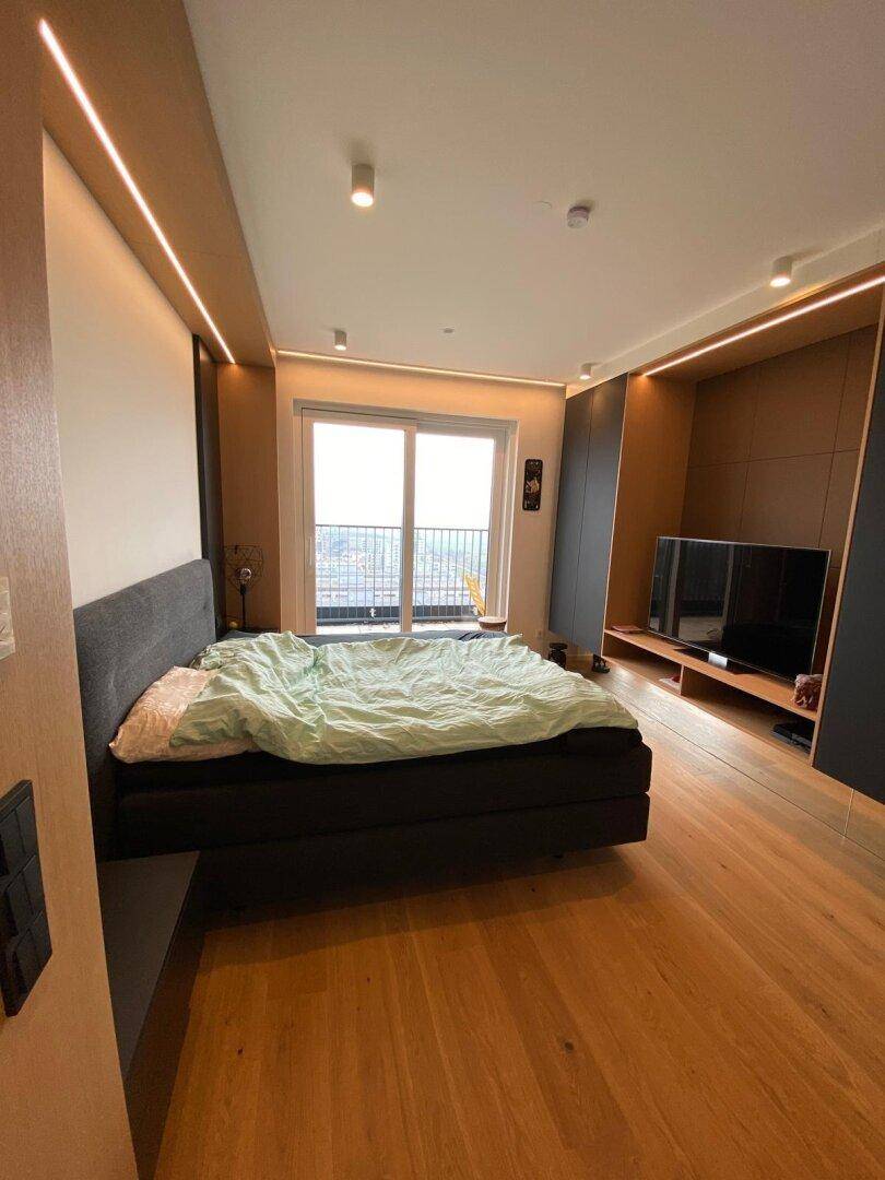 Schlafzimmer mit Holzboden, indirekter Beleuchtung und Zugang zu einem Balkon mit Aussicht.