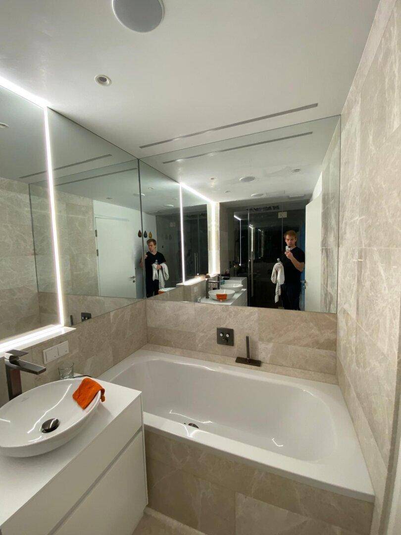 Modernes Badezimmer mit Badewanne, großem Spiegel und indirekter Beleuchtung.