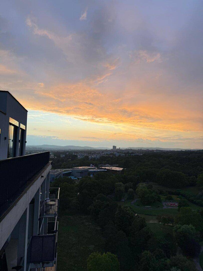Atemberaubender Sonnenuntergang über der Stadt und grünen Wäldern, von einem Balkon aus gesehen.