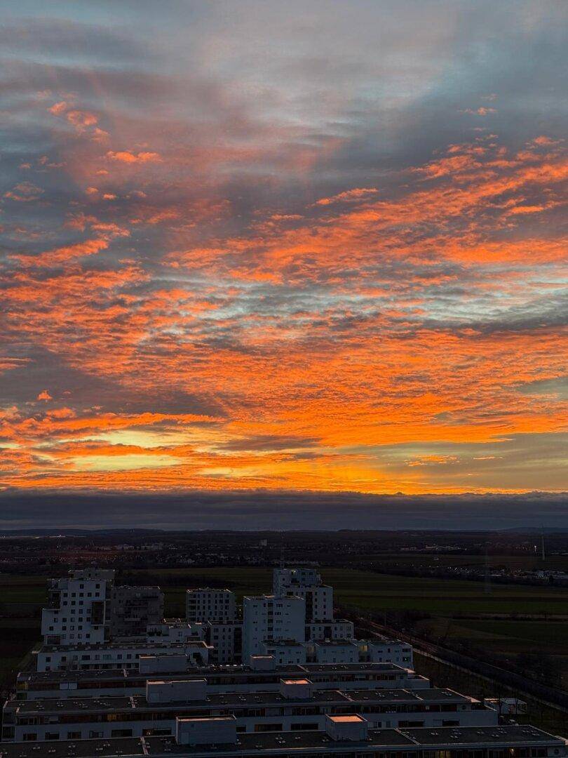 Spektakulärer Sonnenuntergang über der Stadt und der weiten Landschaft mit leuchtend orangefarbenen Wolken.
