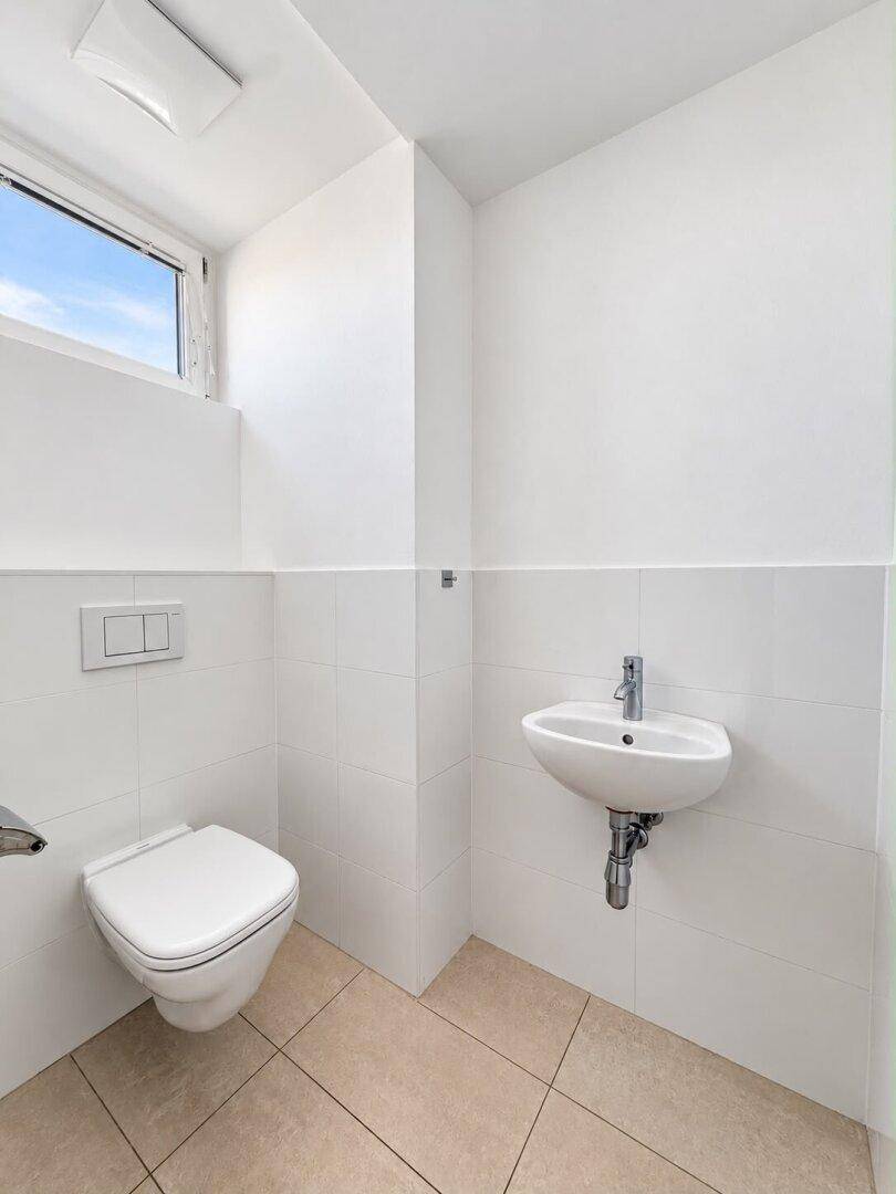 Separates Gäste-WC mit wandhängender Toilette, kleinem Waschbecken und Fenster.