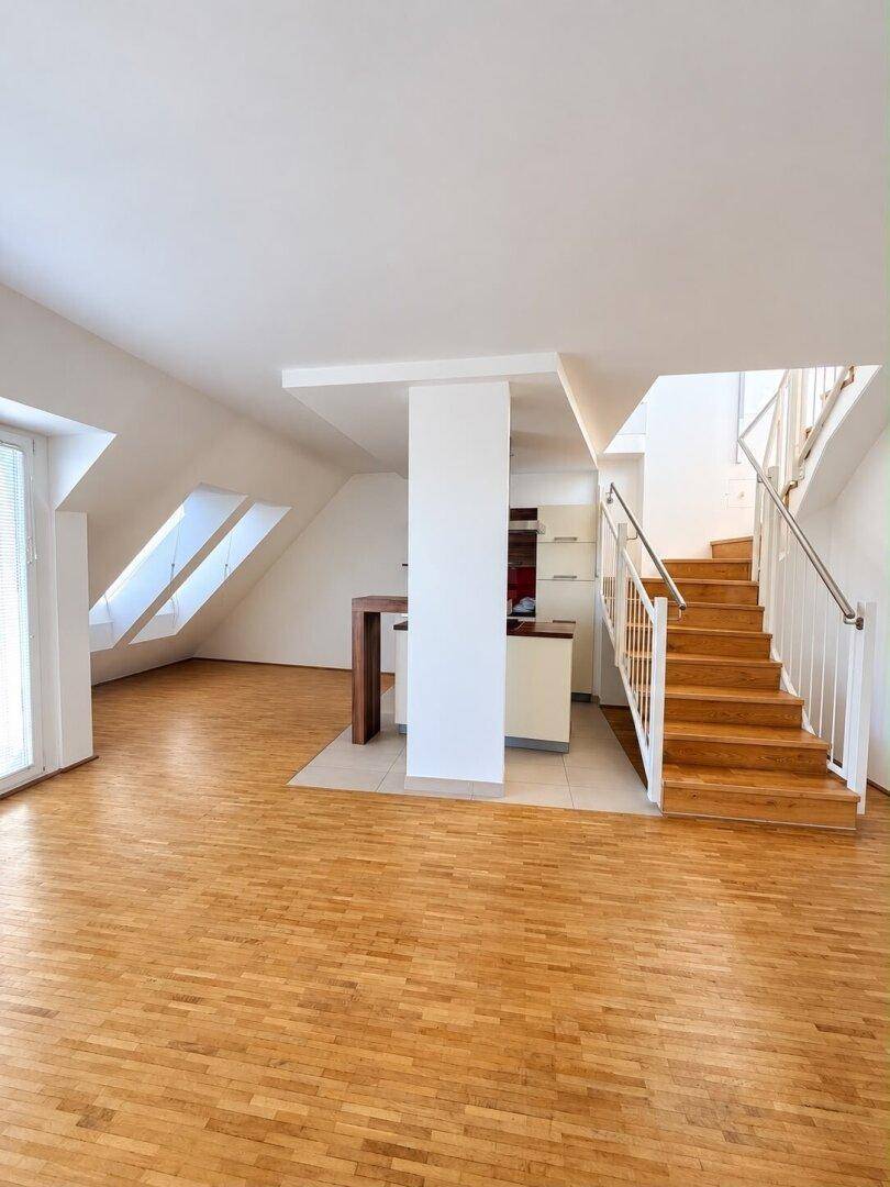 Geräumiger, offener Wohnbereich mit Holzboden, Dachfenstern und integrierter Küchenzeile.