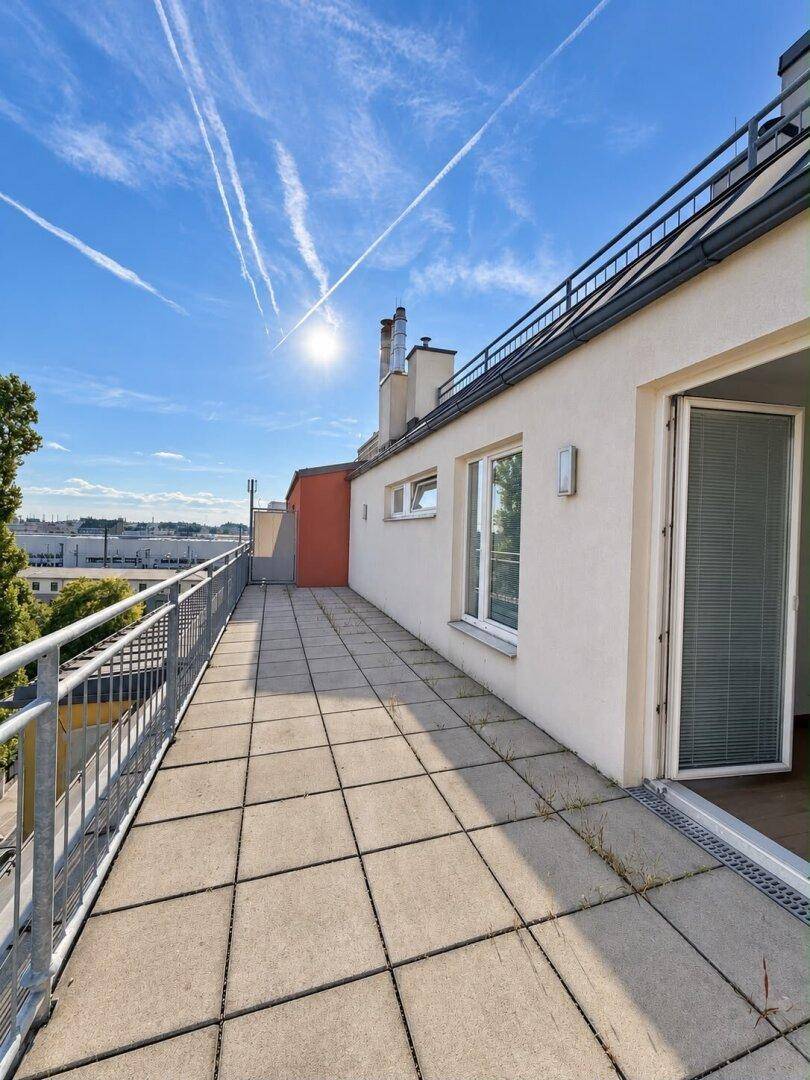 Lange Dachterrasse mit Fliesenboden entlang der Gebäudefassade, bietet viel Platz im Freien.