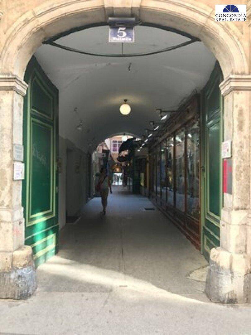 Ein historischer Torbogen führt in eine überdachte Passage mit Geschäften und natürlichem Lichteinfall.