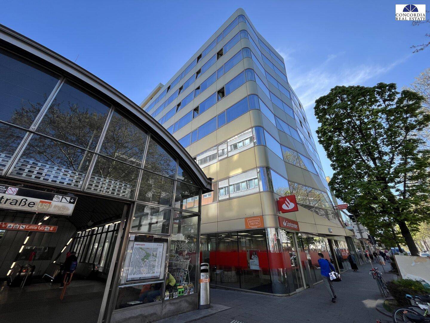 Modernes Bürogebäude mit geschwungener Glasfassade und U-Bahn-Eingang in einer städtischen Umgebung.